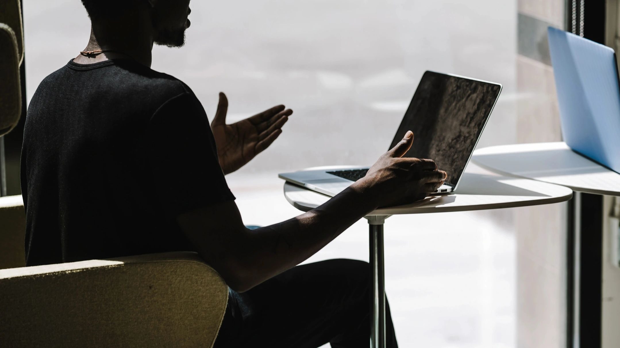 Frustrated man sitting with his hands in the air in front of his laptop.