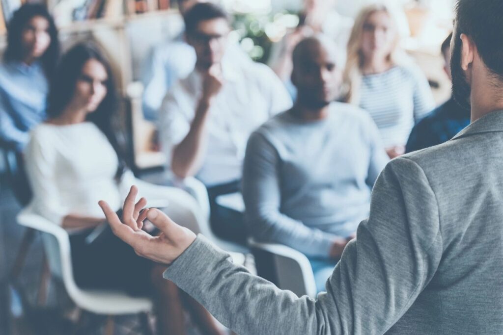 Speaker addressing an engaged audience in a seminar or training session, with listeners focusing on the presentation.