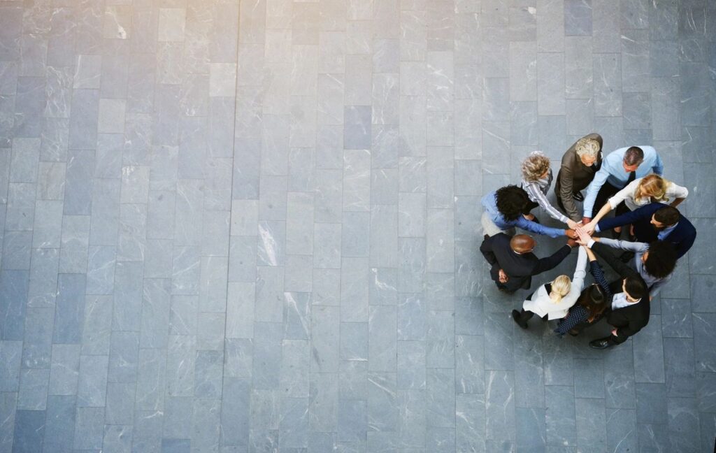 Group of people standing in a circle with their hands joined in the center, symbolizing teamwork, unity, and a coordinated incident response, viewed from above.