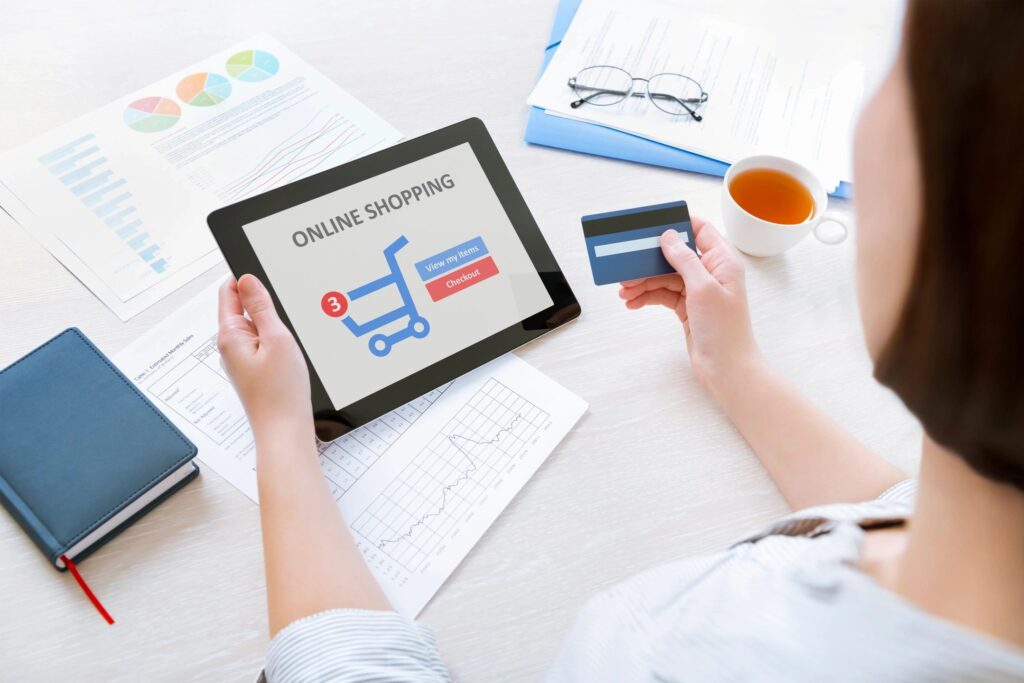 A person shopping online using a tablet and credit card, with documents and a cup of coffee on the desk. The scene relates to Seasonal Cyber Safety Tips for the Holidays, emphasizing the importance of securing online transactions during festive shopping.